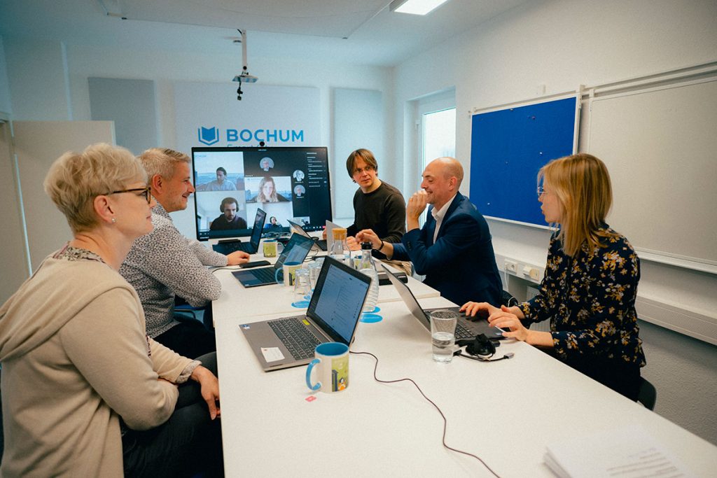 Personen im Besprechungsraum mit Laptops und Präsentation.
