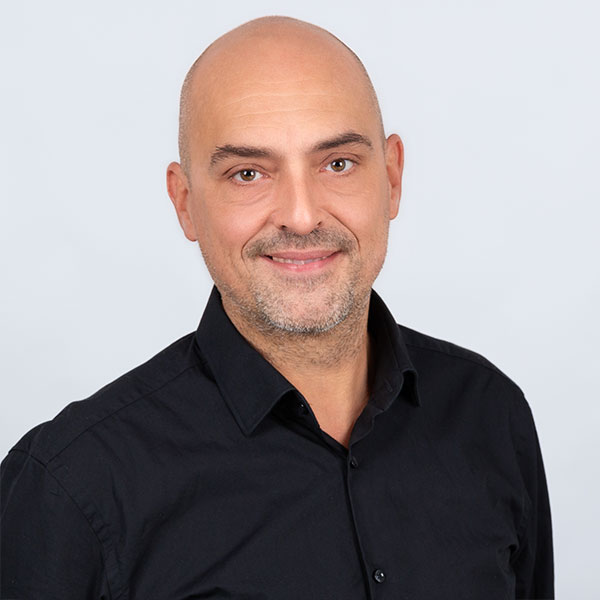 orträt eines Mannes mit Glatze und freundlichem Lächeln, gekleidet in ein schwarzes Hemd.