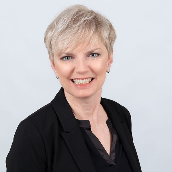 Eine lächelnde Frau mit kurzem, blondem Haar in einem schwarzen Blazer.