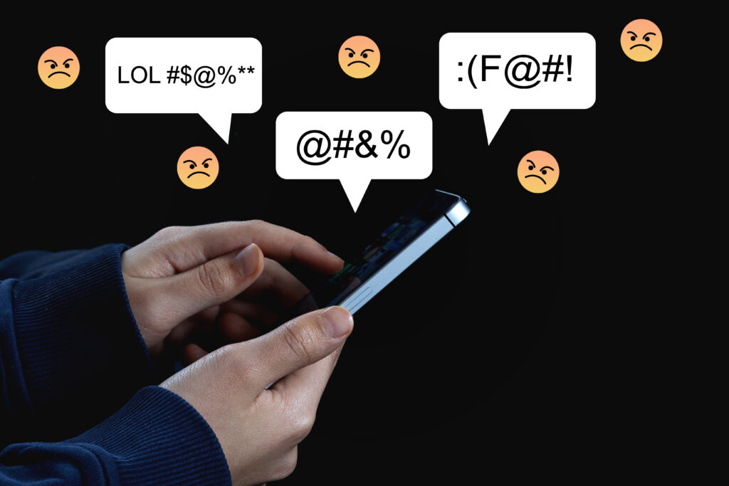 Symbolbild für Hassrede im Netz – Smartphone mit Emojis und beleidigenden Begriffen.