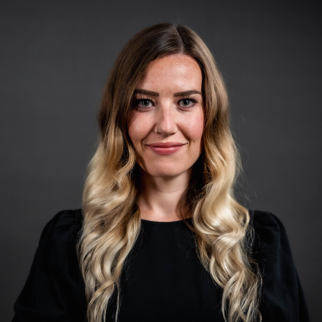 Porträt einer Frau mit langen, blonden Haaren und schwarzem Oberteil.