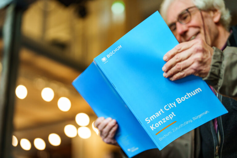 Person hält eine geöffnete blaue Broschüre mit dem Titel „Smart City Bochum“.